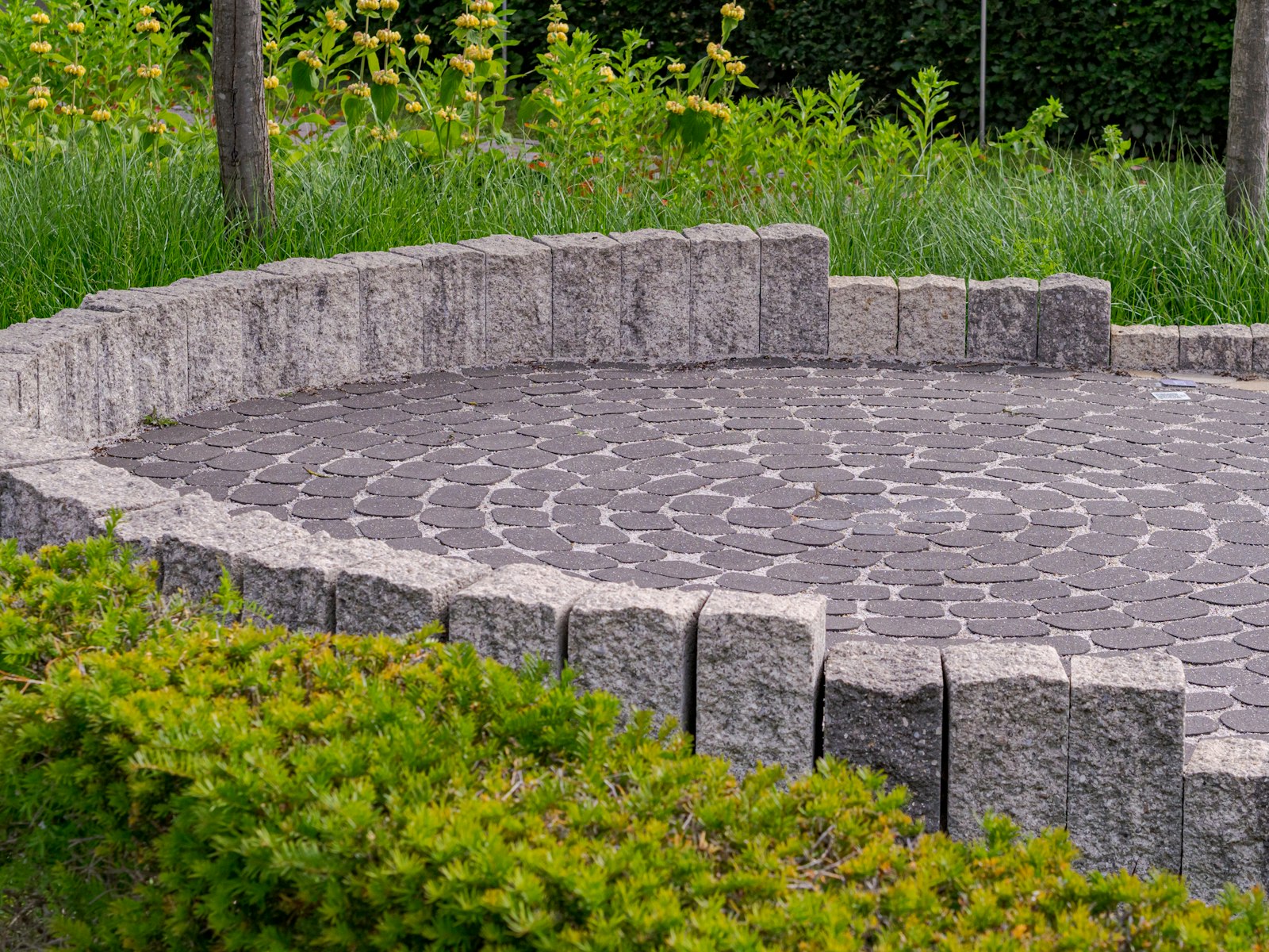 A curved paver patio with a low stone wall bordering a green lawn